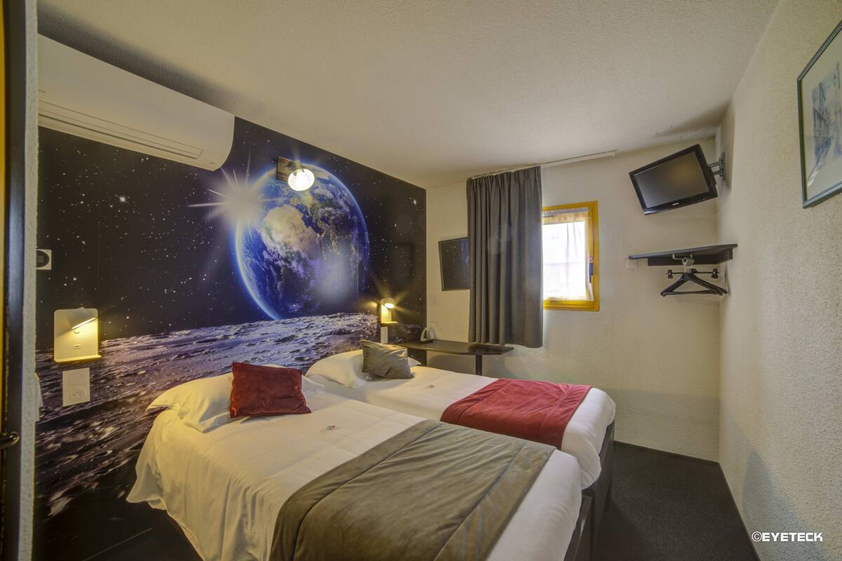 A hotel room with two beds, a large space-themed mural on the wall, a flat-screen TV mounted on the wall, and a window with curtains.
