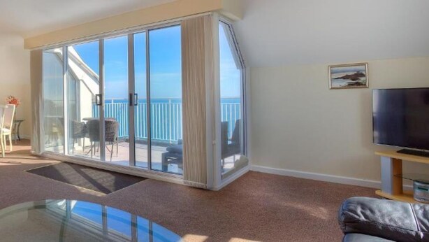 A living room with a sofa, a glass coffee table, a TV, and a balcony with a view of the sea. - Hotel Jerbourg (St. Martins)