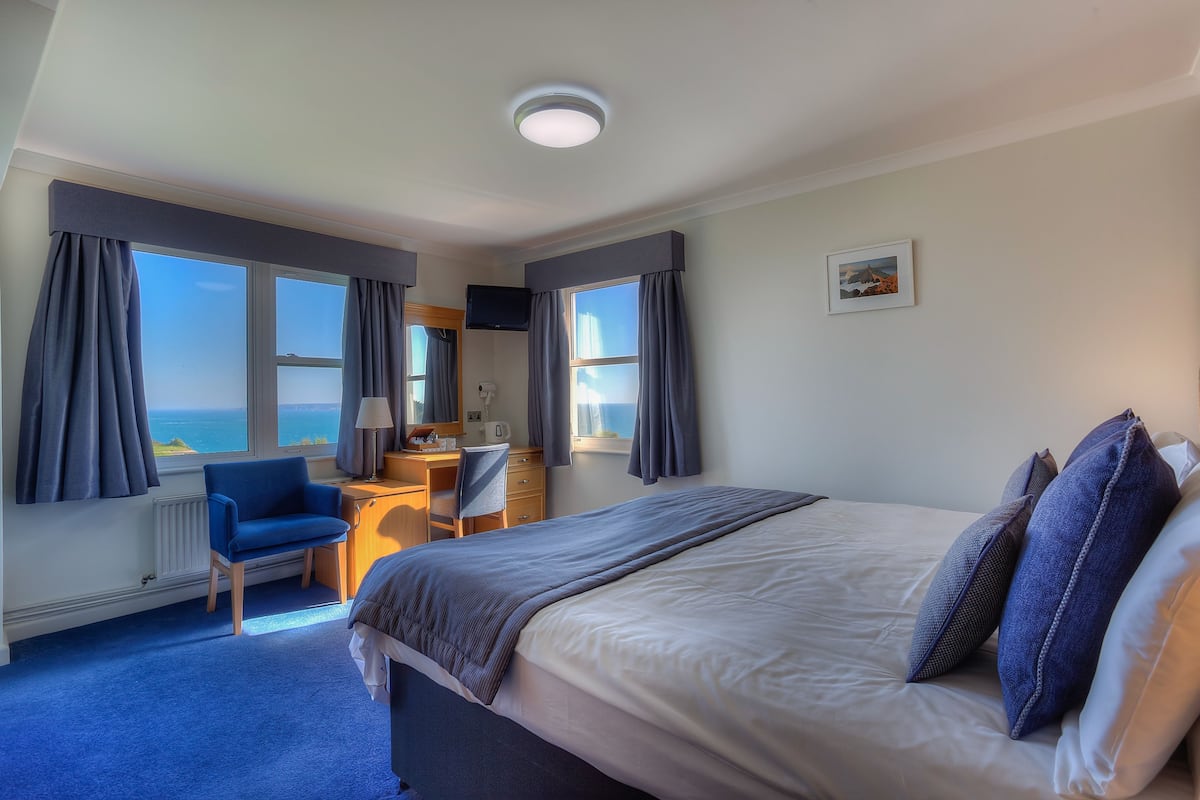 Habitación de hotel con una cama grande, un escritorio, una silla y vista al mar.