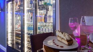 A dessert on a plate with a slice of cake and a glass of pink drink on a table. - Hotel Jerbourg (St. Martins)