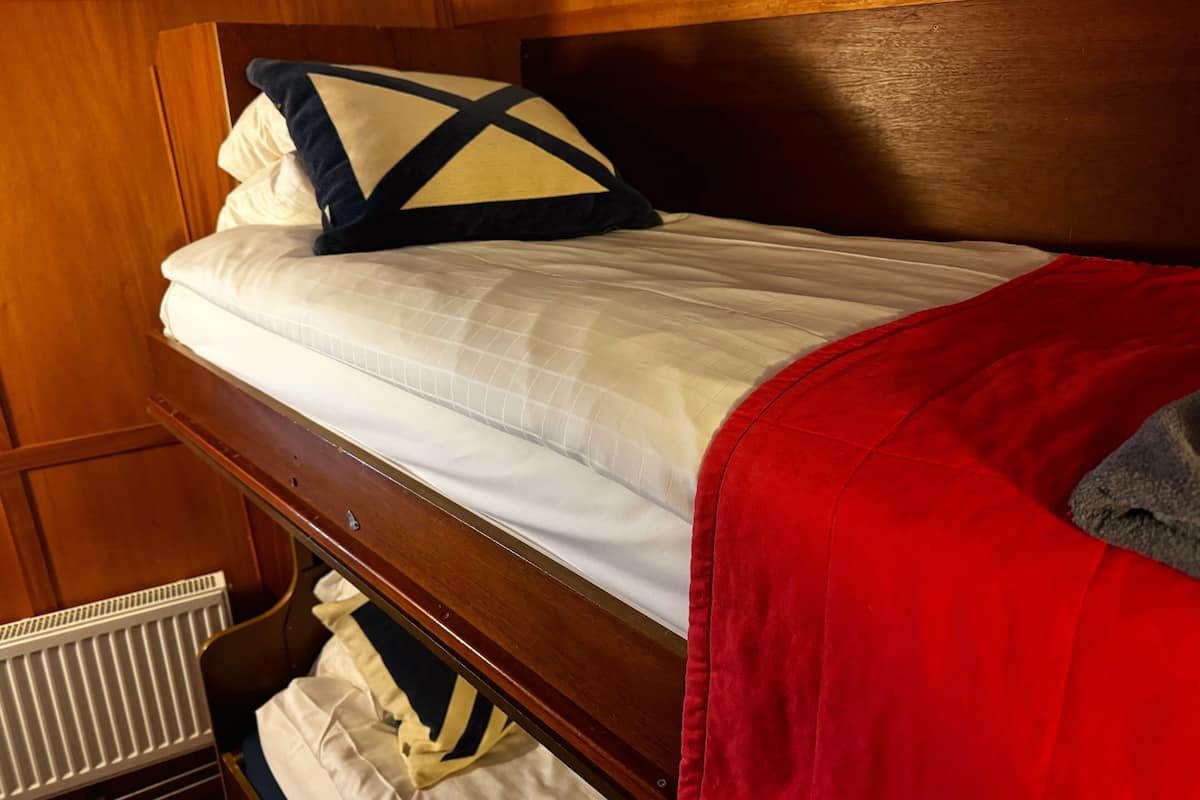 Een stapelbed met een witte matras en een rode deken.