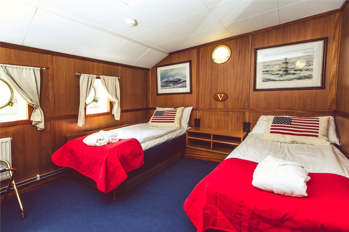 Een hotelkamer met twee bedden, elk met een rode deken en een kussen met een Amerikaanse vlag. De kamer heeft houten lambrisering, een raam met gordijnen en een ingelijst schilderij aan de muur.