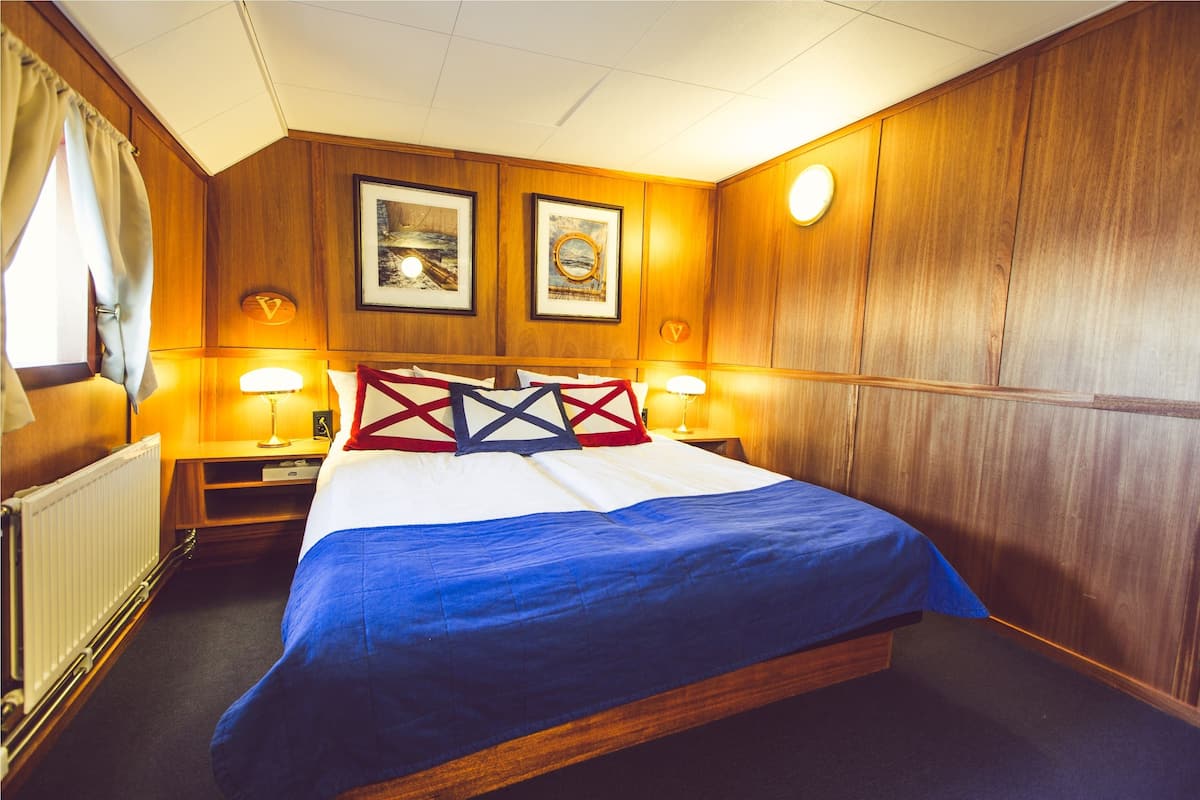 Een hotelkamer met een houten wandpaneel, een bed met een blauw-witte spreideken, twee ingekaderde foto's en twee bedlampjes.