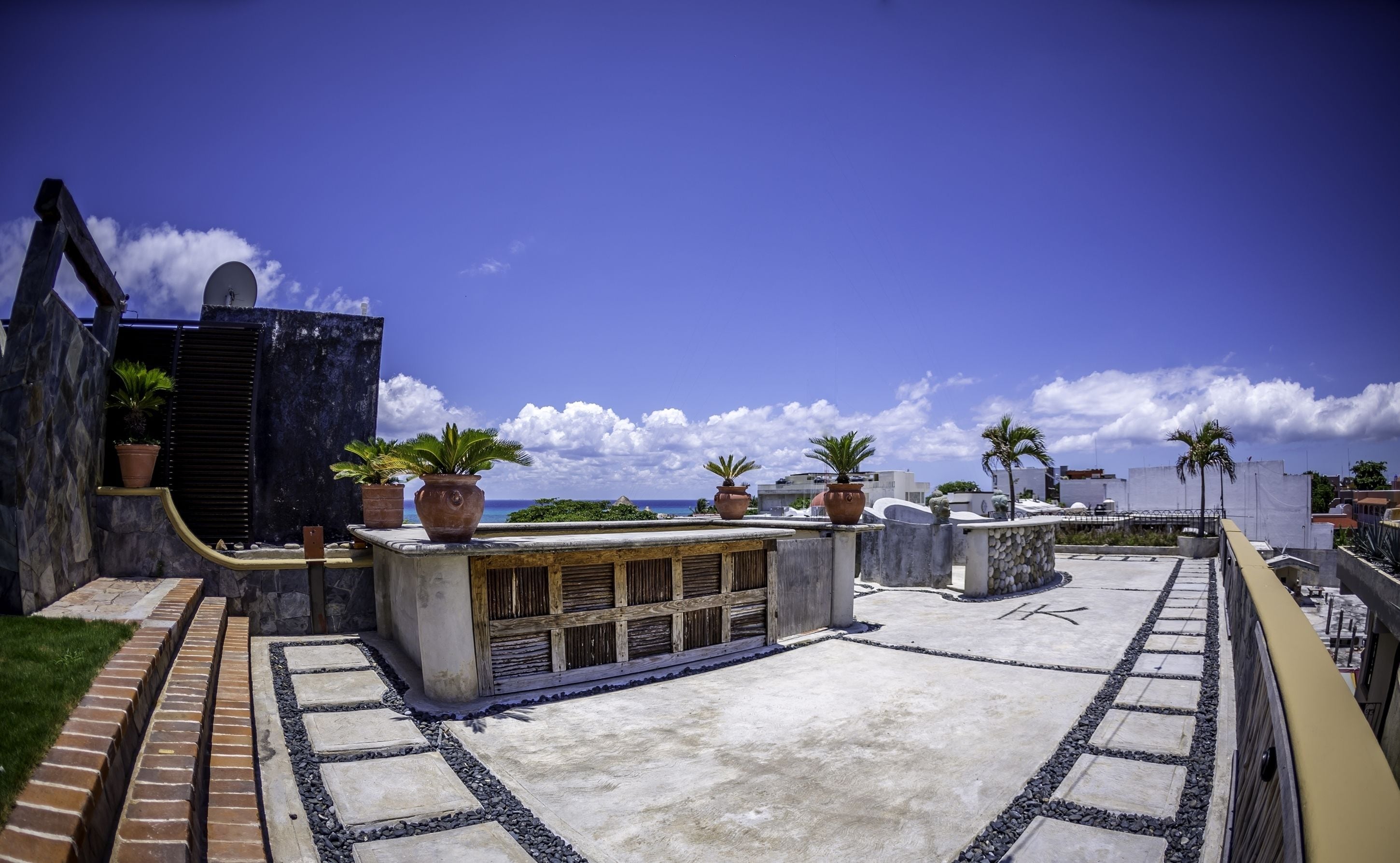 A rooftop terrace with potted plants, a concrete pathway, and a view of the ocean.