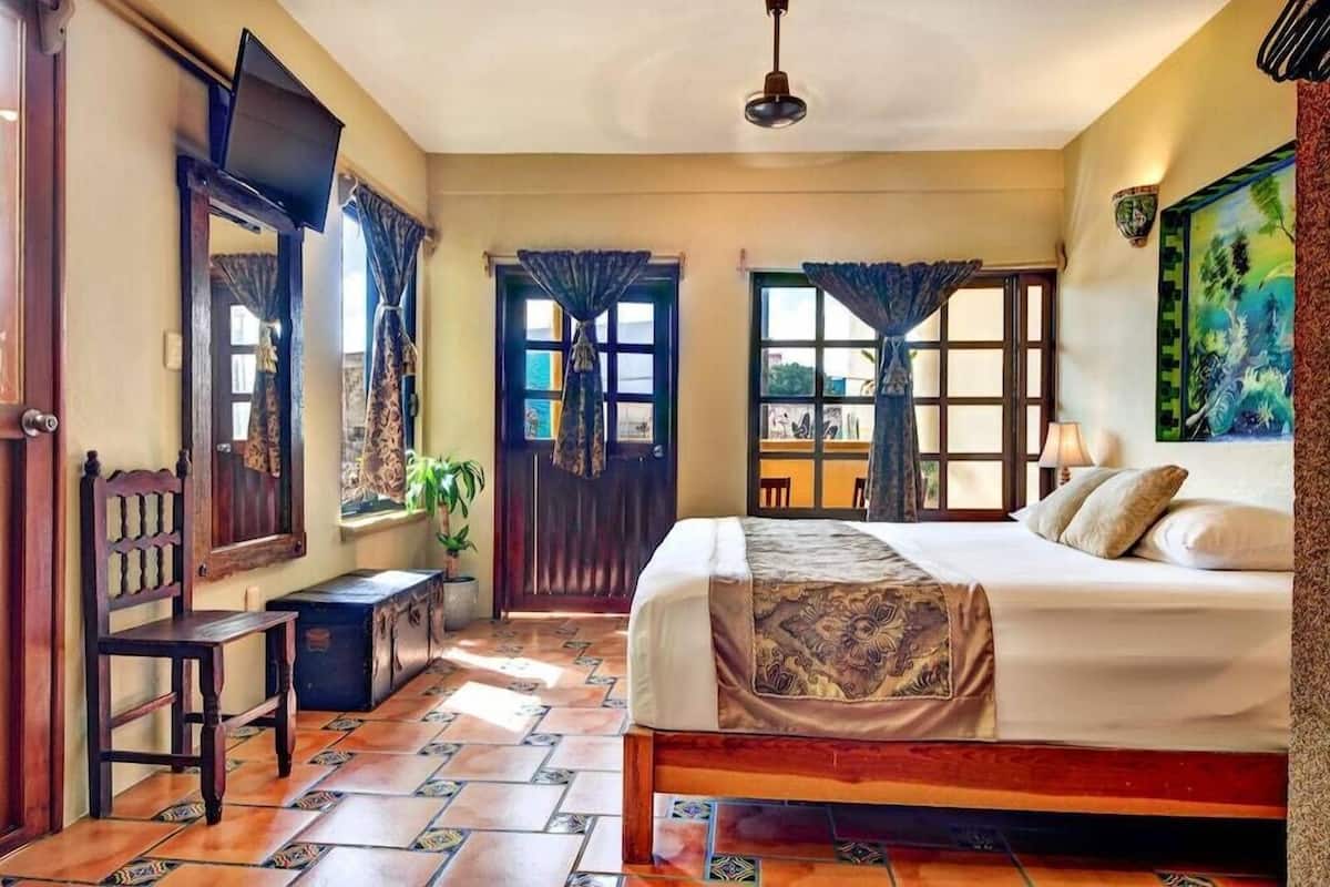 A bedroom with a bed, a chair, a desk, a window with curtains, and a door.