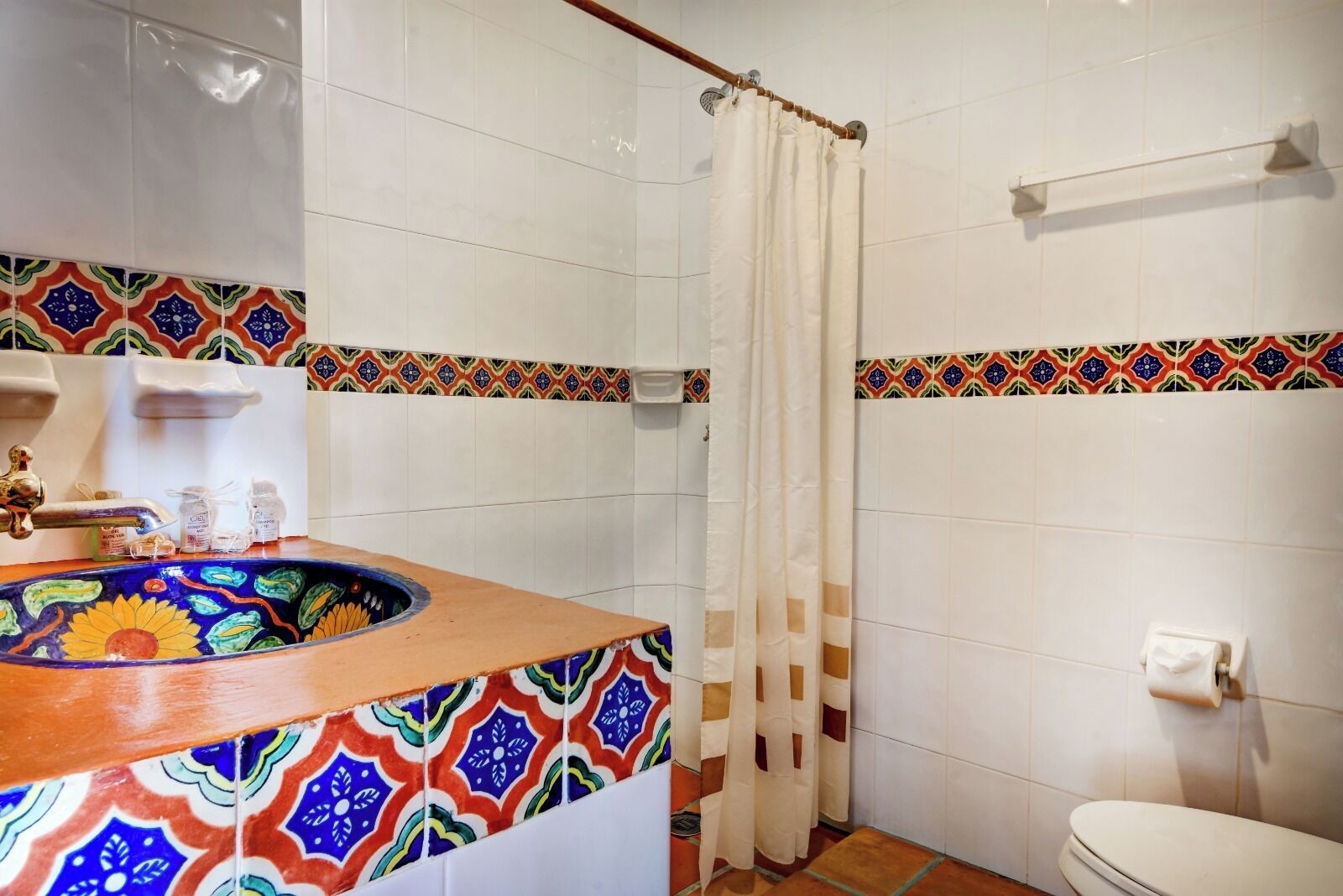 A bathroom with a colorful sink, white tiles, a shower curtain, and a toilet.