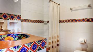 A bathroom with a colorful sink, white tiles, a shower curtain, and a toilet.