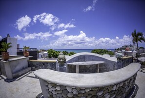 A rooftop terrace with a Buddha statue, potted plants, and a view of the ocean.