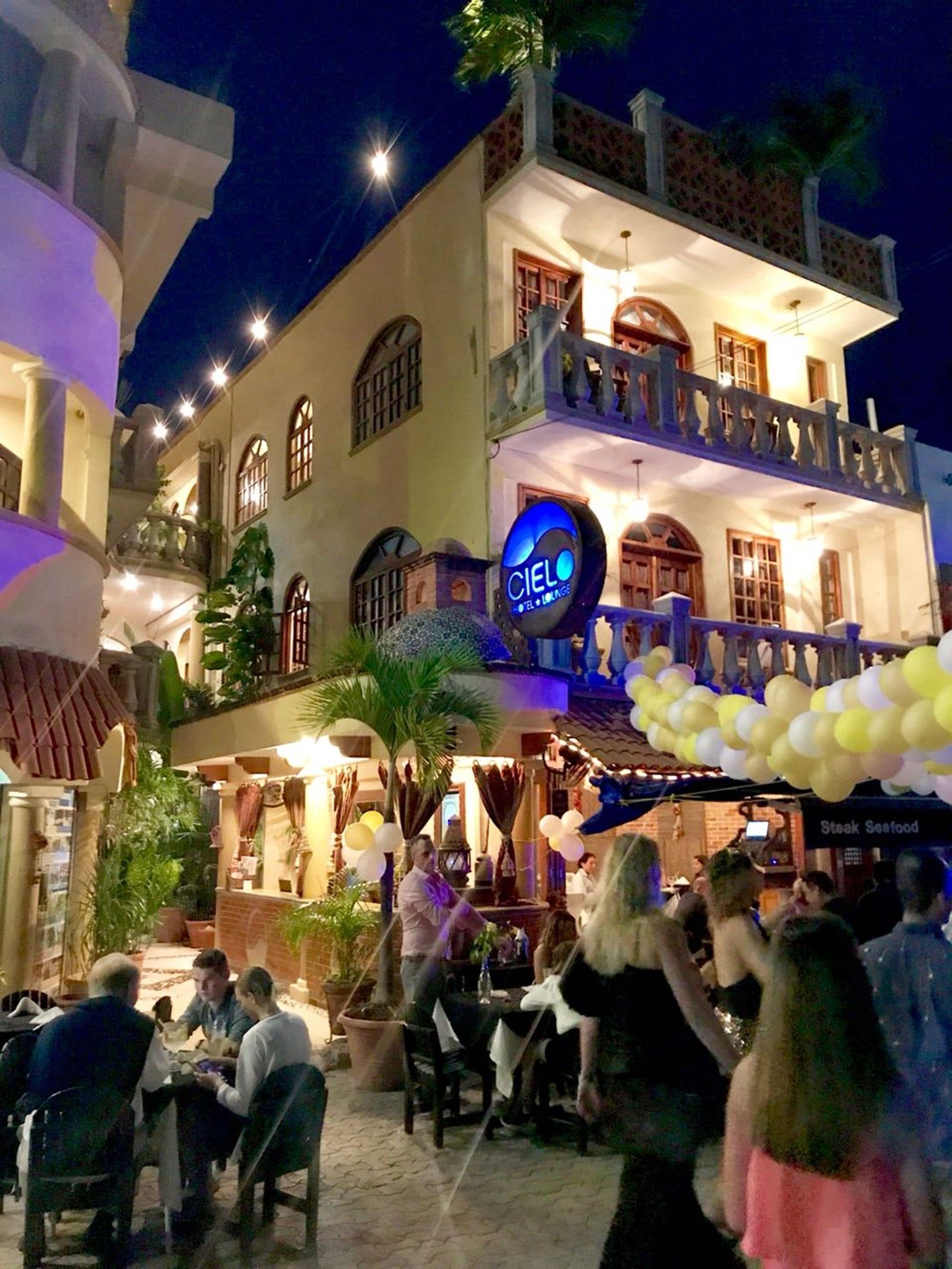Um hotel com área de estar ao ar livre, um letreiro com 'Cielo Hotel & Lounge' e uma varanda com grades decorativas.