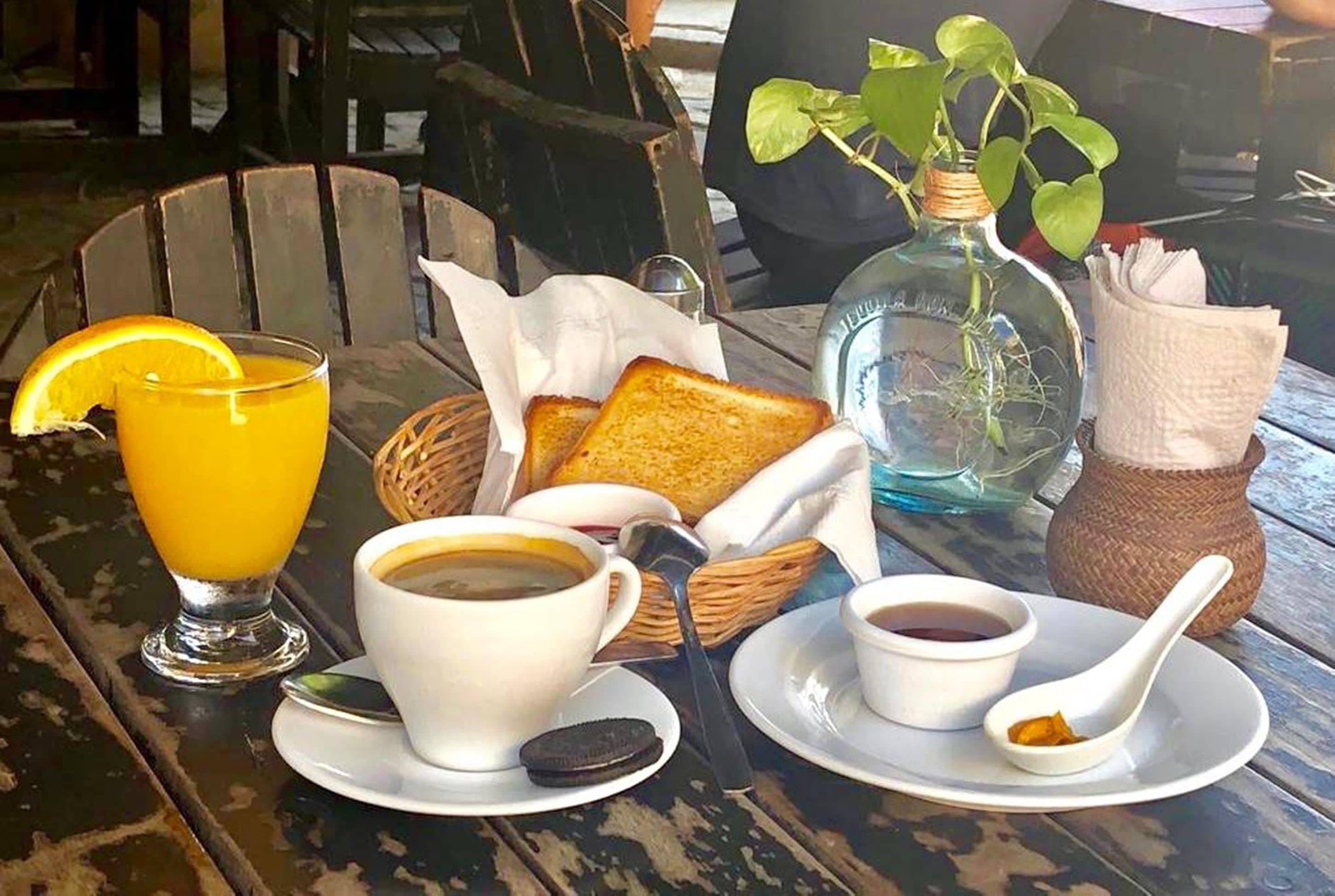 Un esmorzar amb torrades, suc d'aranja, cafè i una planta sobre una taula de fusta.