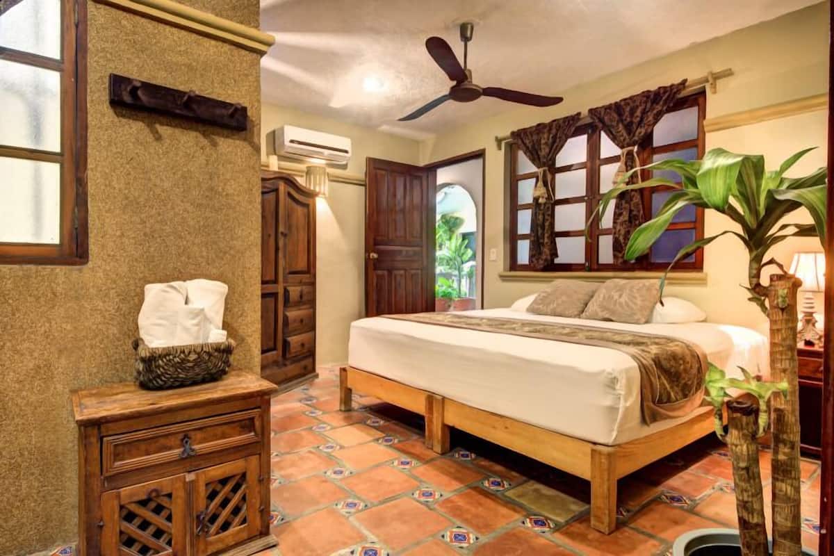 A bedroom with a wooden bed, a ceiling fan, a window with curtains, and a potted plant.