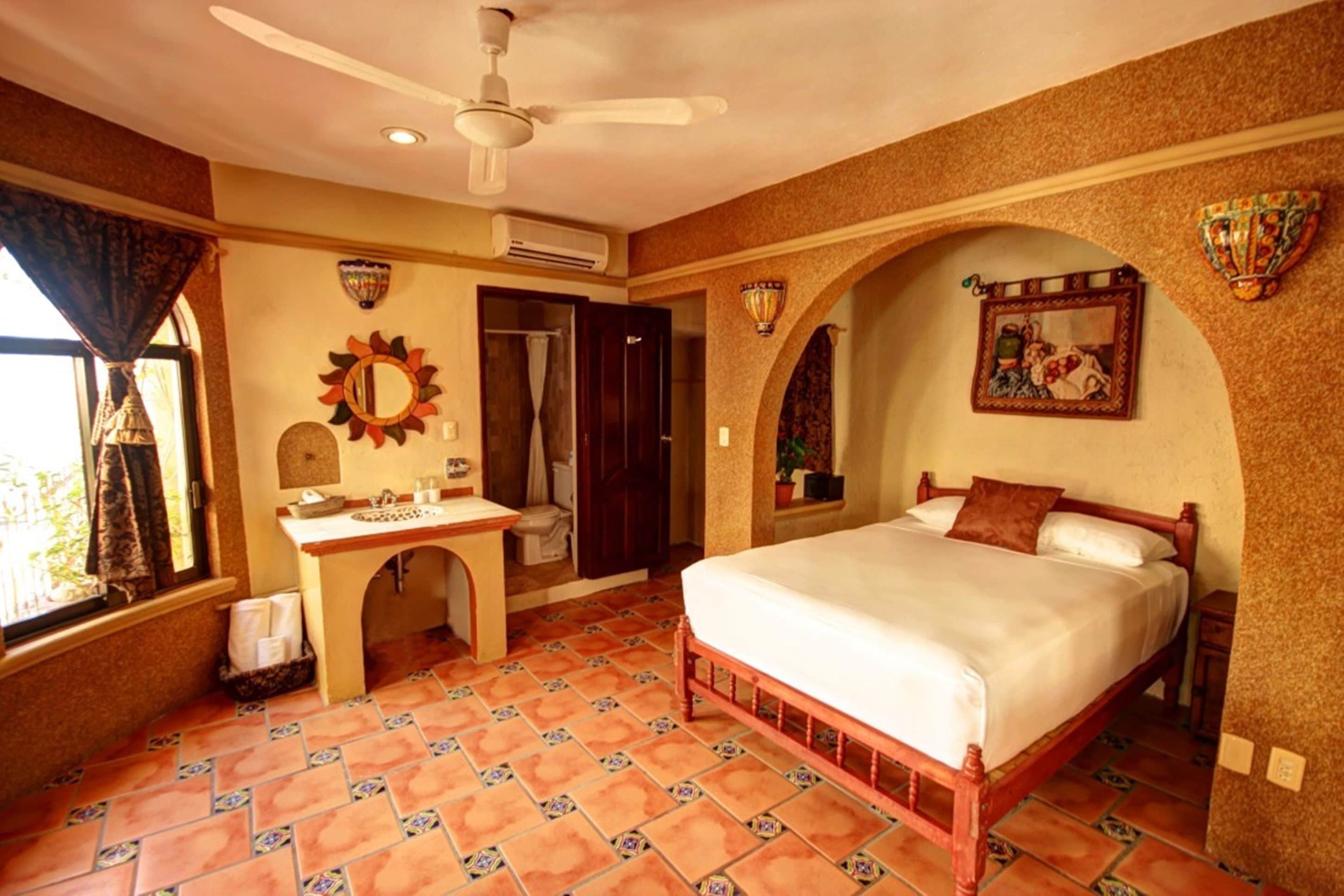 A bedroom with a bed, a vanity with a mirror, a ceiling fan, and a window with curtains.