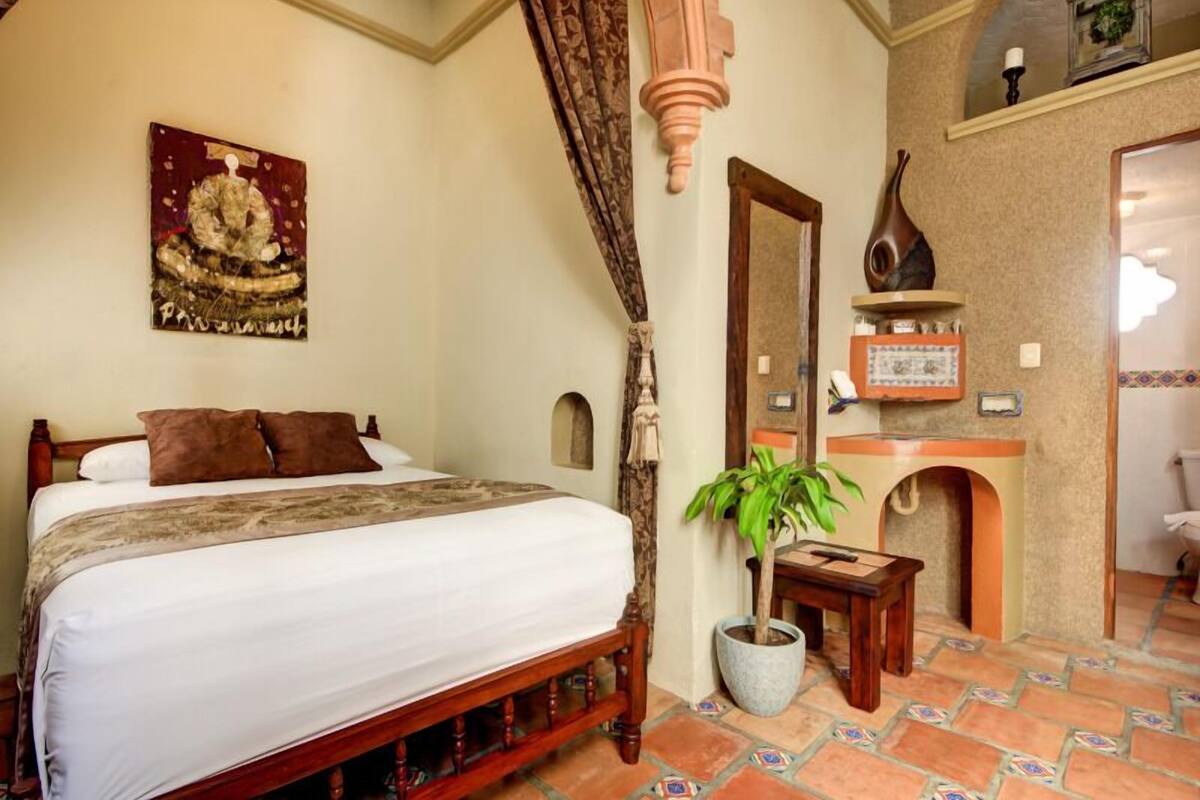 A bedroom with a wooden bed, a potted plant, a mirror, and a wall-mounted shelf with decorative items.
