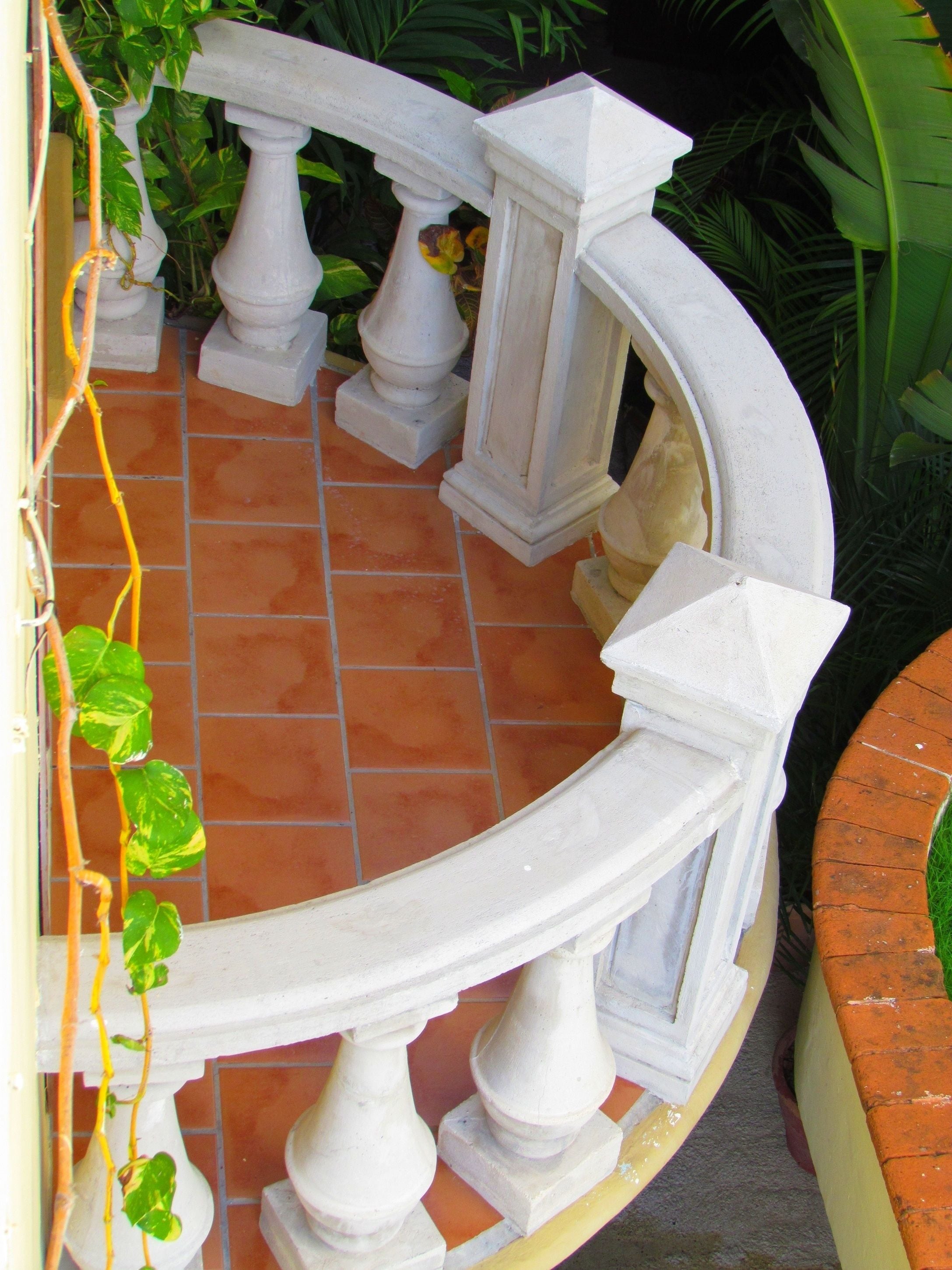 A white balustrade with a curved design, terracotta tiles, and green foliage.