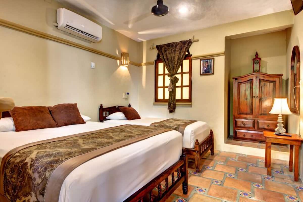 A hotel room with two beds, a wooden wardrobe, a window with curtains, and a tiled floor.