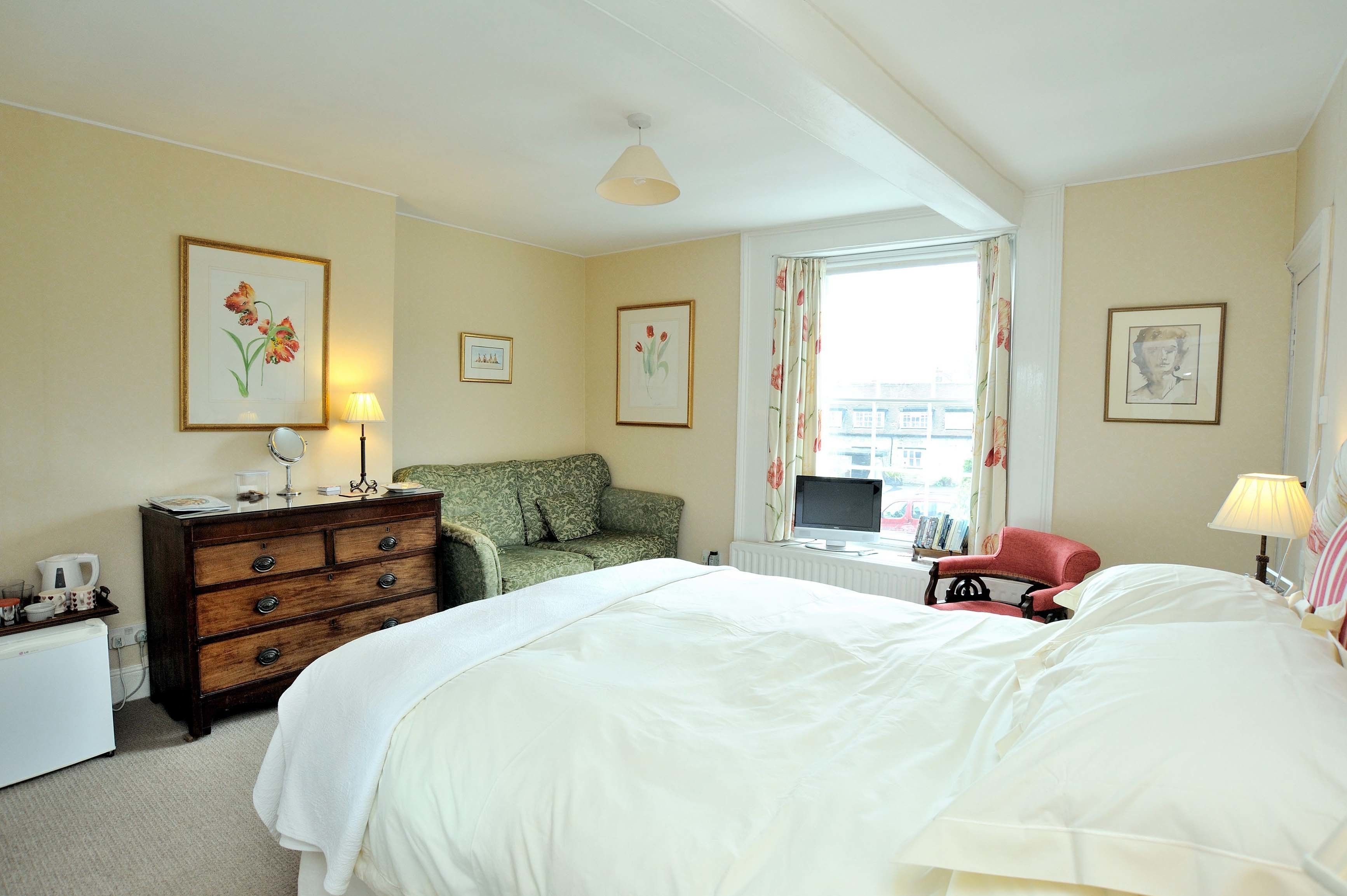 A hotel room with a large bed, a dresser, a green sofa, a red armchair, and a window with curtains.