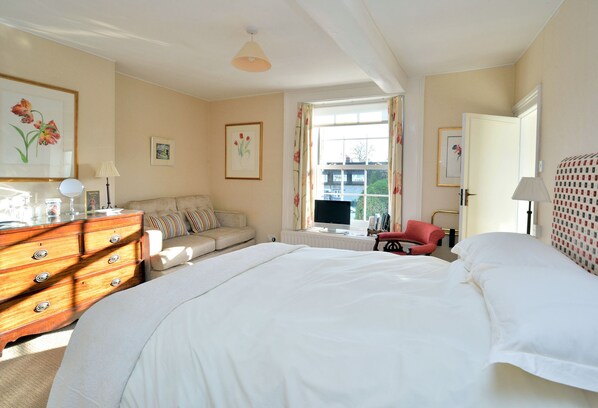 A bedroom with a large bed, a dresser, a sofa, a chair, and a window with curtains.