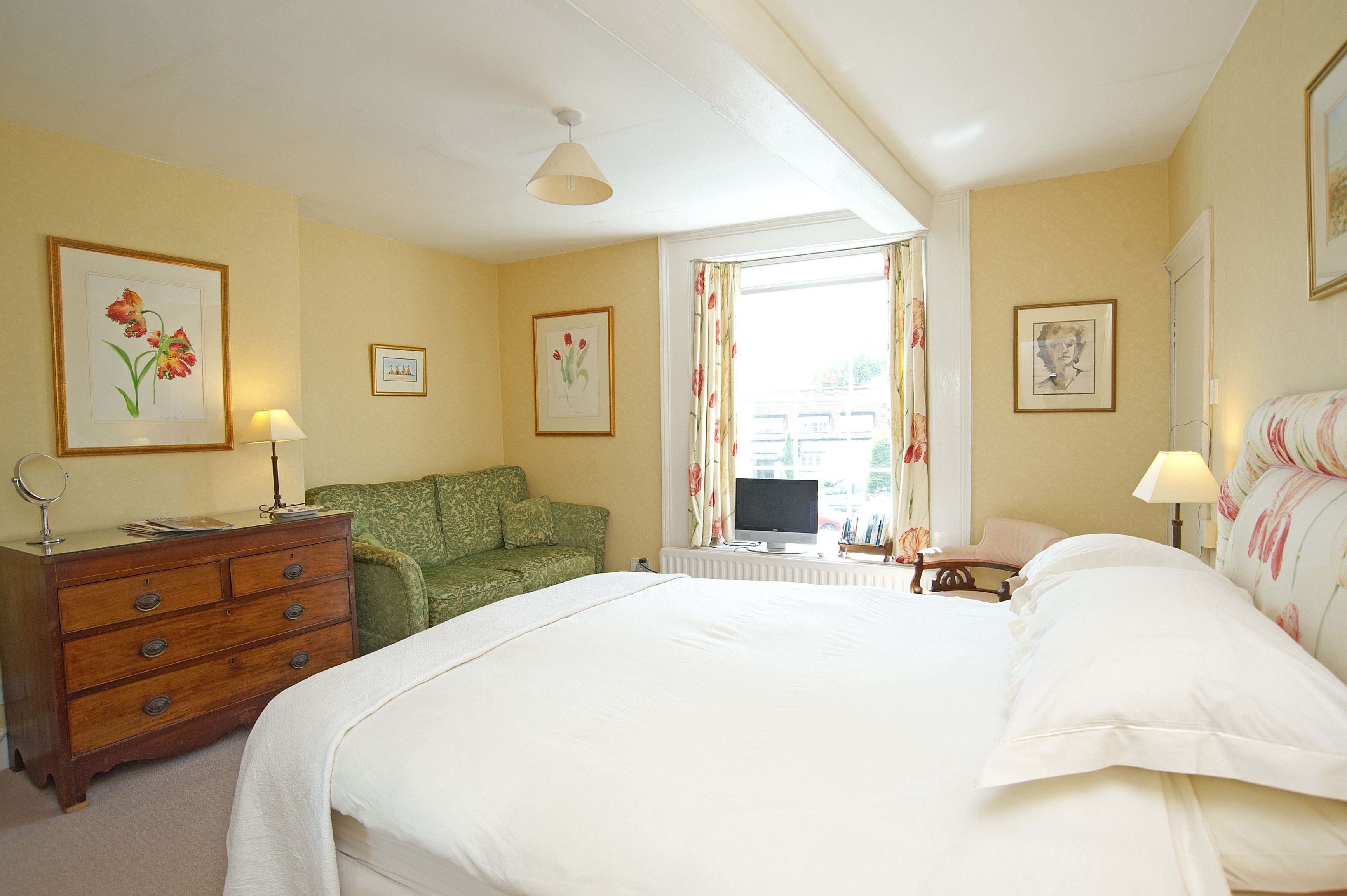 Een hotelkamer met een groot bed, een groene bank, een houten dressoir, een televisie en beeldelementen aan de muur.