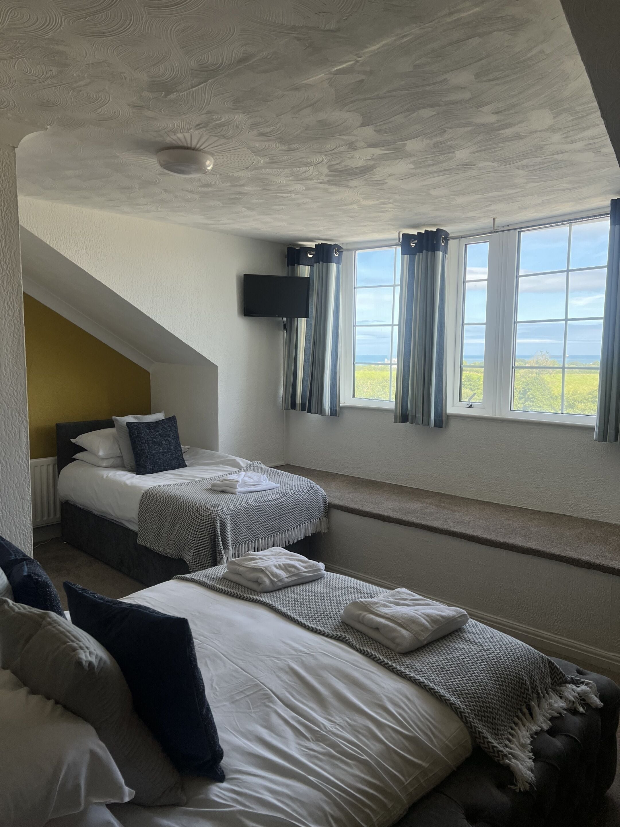 Een hotelkamer met twee bedden, een aan de muur bevestigde televisie en een raam met gordijnen.
