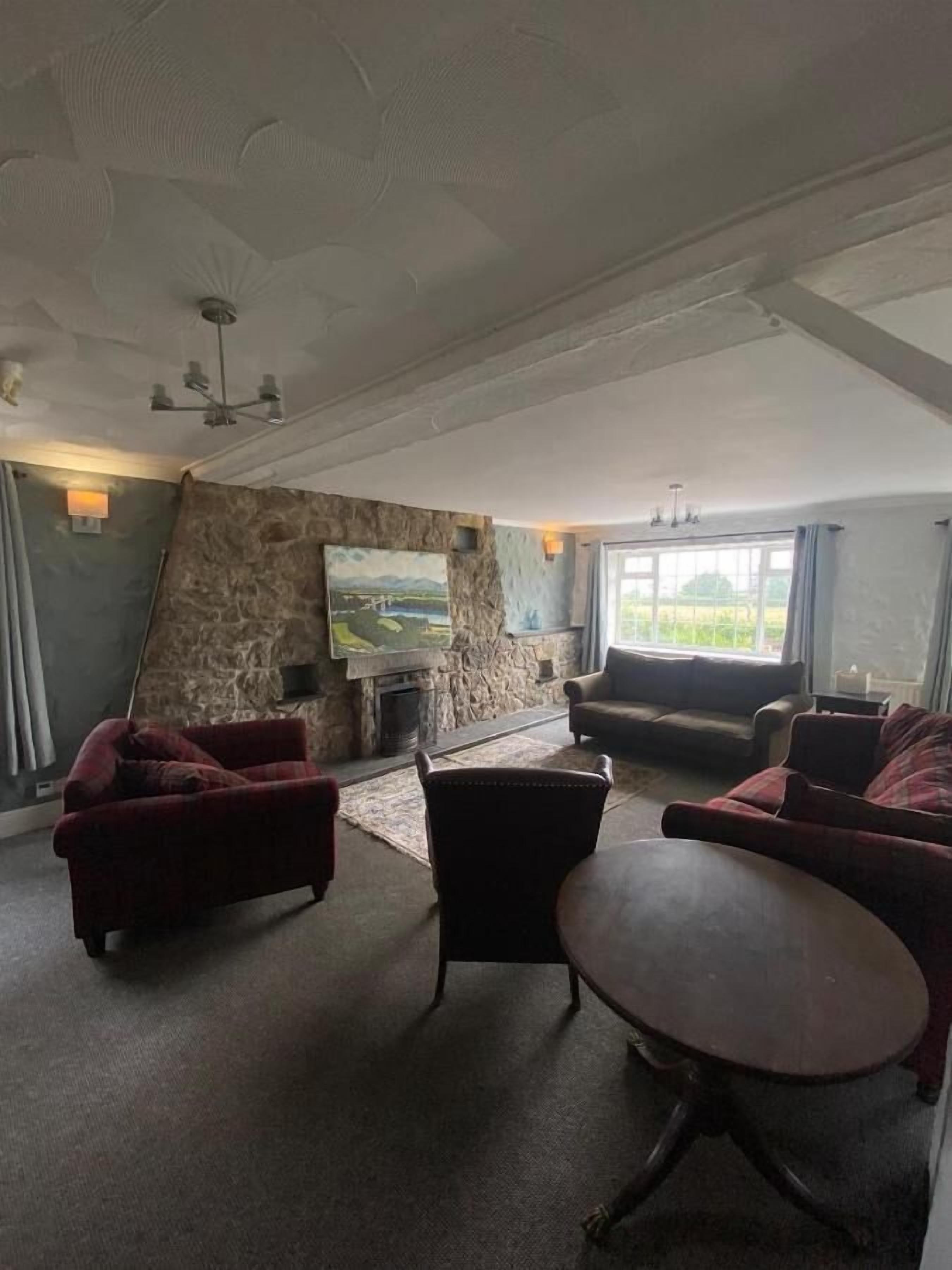 A spacious living room with a stone wall, a fireplace, and a large window offering a view of greenery.
