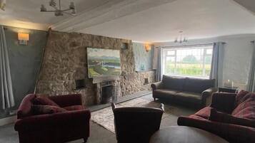 A spacious living room with a stone wall, a fireplace, and a large window offering a view of greenery.