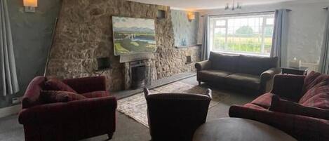 Un salón espacioso con pared de piedra, chimenea y un gran ventanal con vistas al verdor.