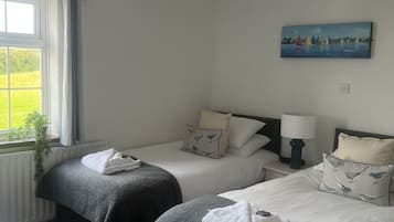 A hotel room with two single beds, a window with curtains, a painting on the wall, and a radiator.