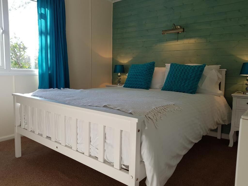 Un lit blanc avec des oreillers bleus et blancs, une tête de lit turquoise et une table de chevet avec une lampe.
