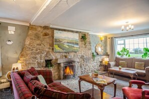 Ein gemütliches Wohnzimmer mit Kamin aus Stein, einer Couch, einem Couchtisch und einem Landschaftsbild.