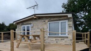 A stone building with a wooden deck, a picnic table, and a rope enclosure.