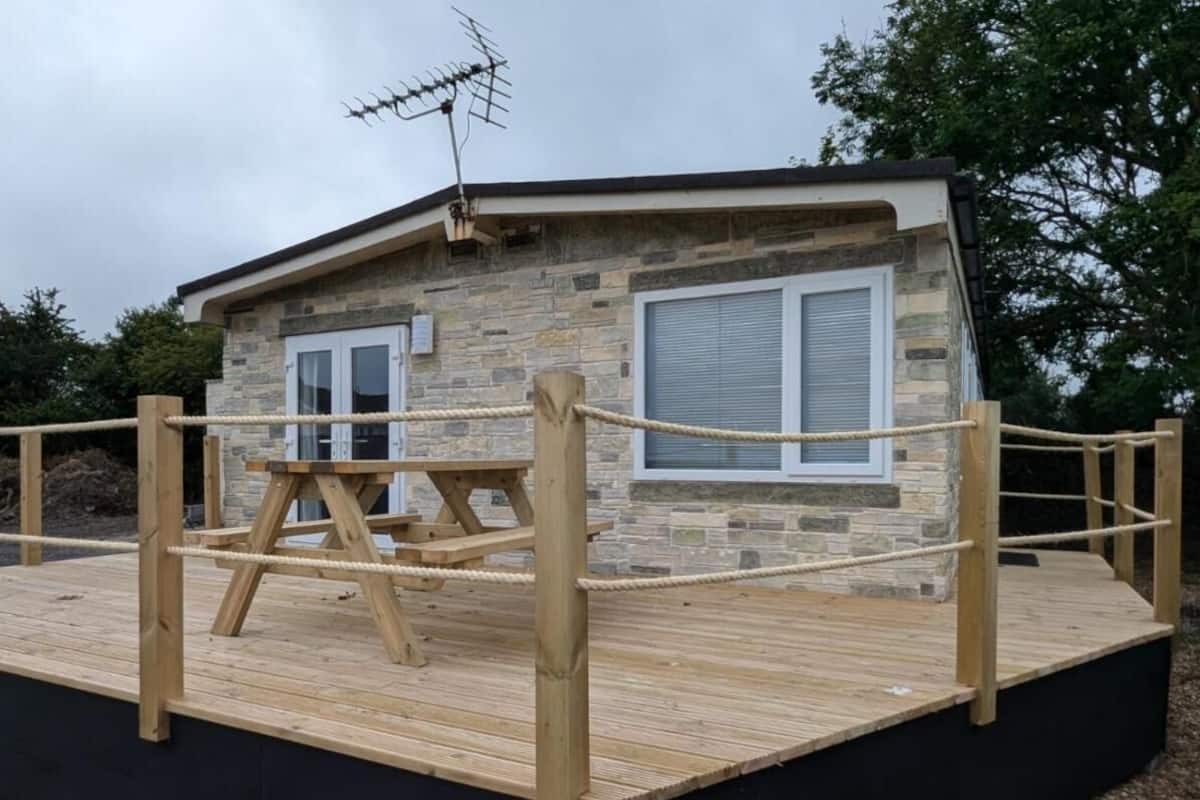 A stone building with a wooden deck, a picnic table, and a rope enclosure.