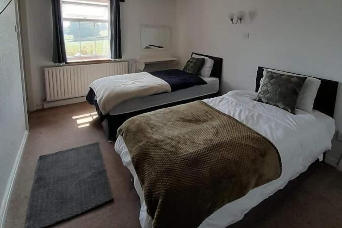 A hotel room with two single beds, a window with curtains, a radiator, and a small rug.