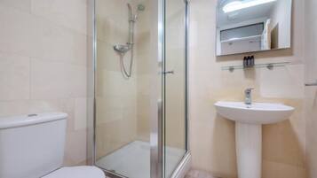 Un baño con ducha de vidrio, lavamanos blanco y retrete.