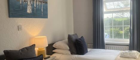 A hotel room with two beds, a painting of sailboats, a lamp, and a window with curtains.