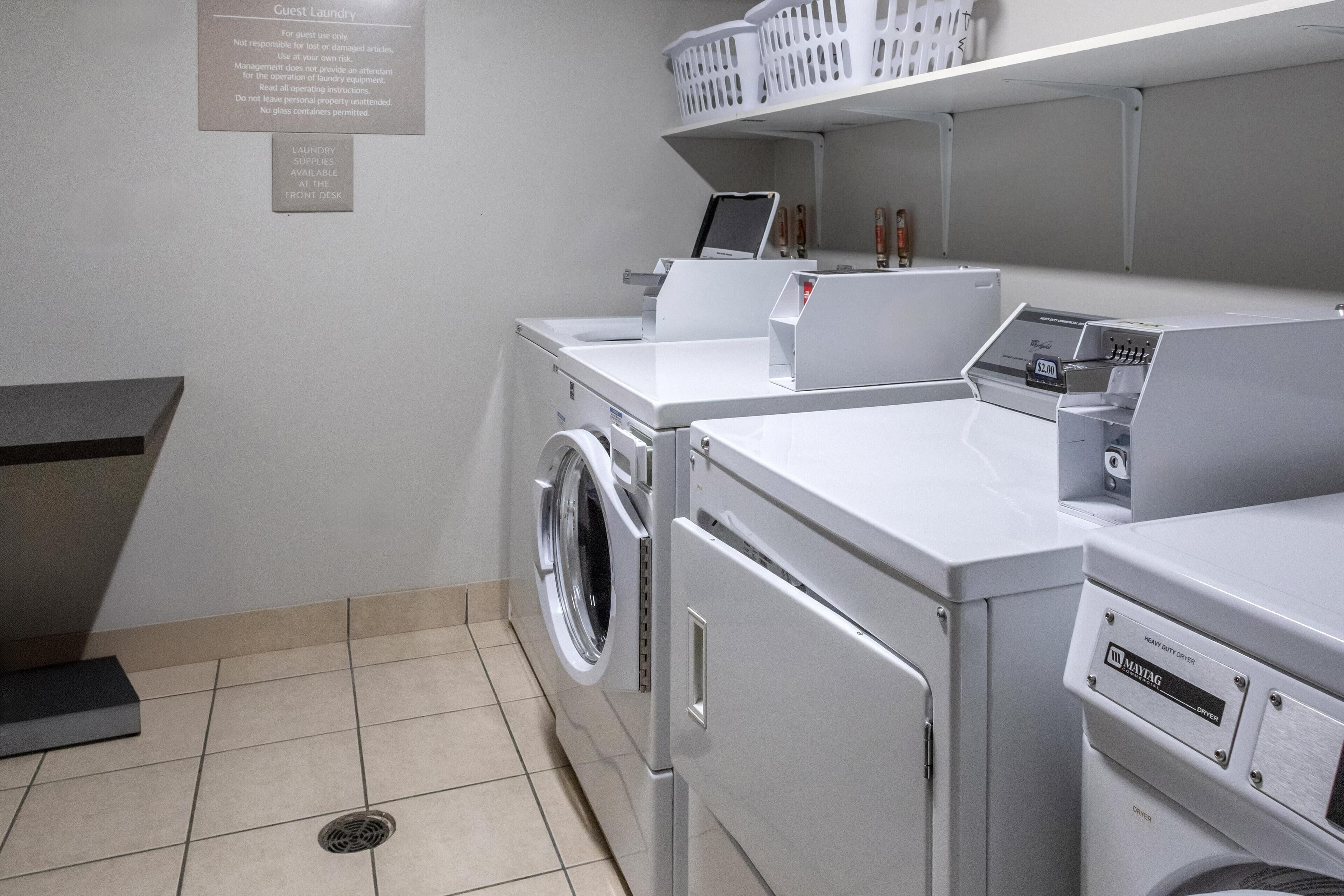 A hotel laundry room with a front desk, washing machines, and a shelf with laundry supplies.