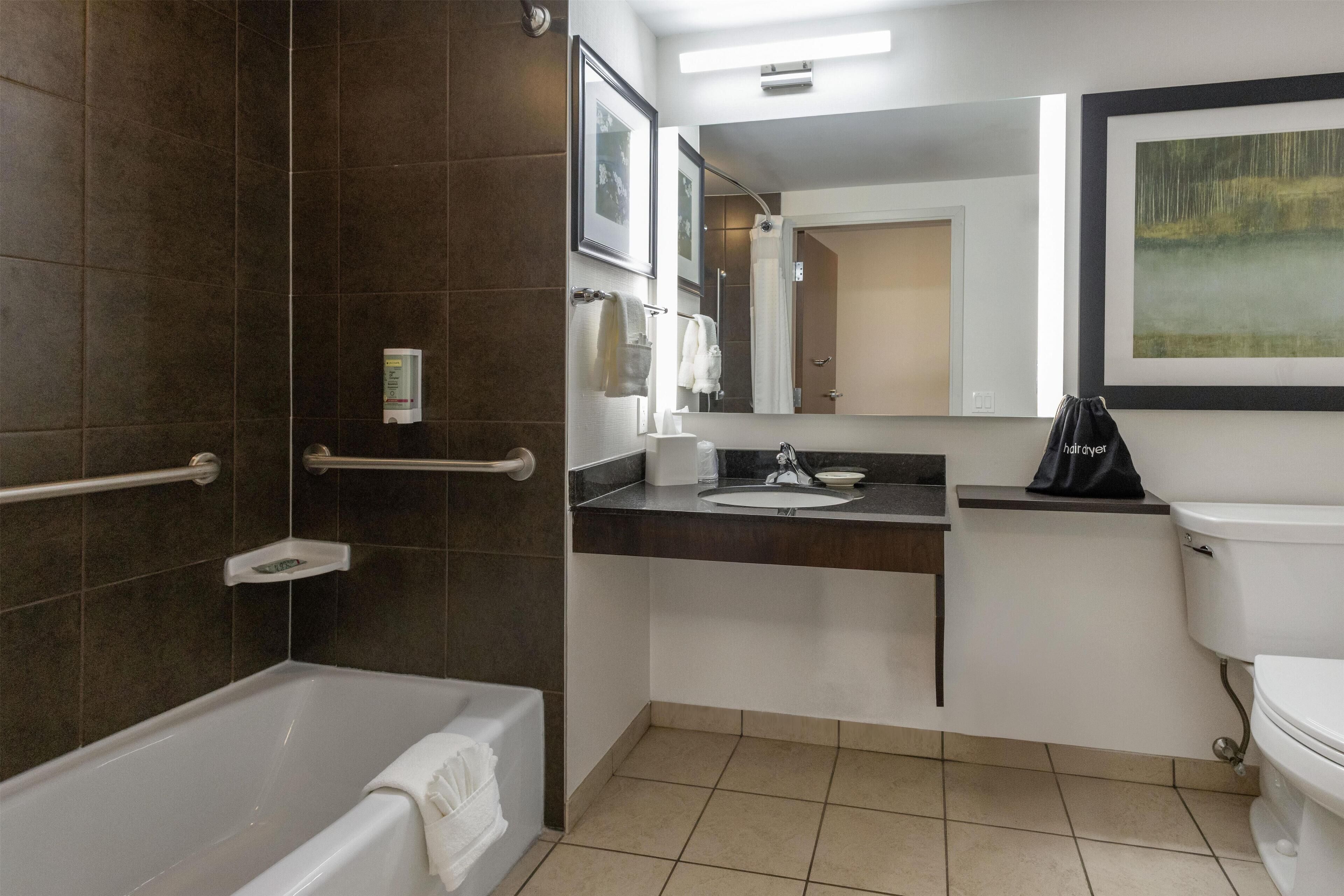 A modern bathroom with a bathtub, a sink, and a toilet. There are towels and toiletries visible.