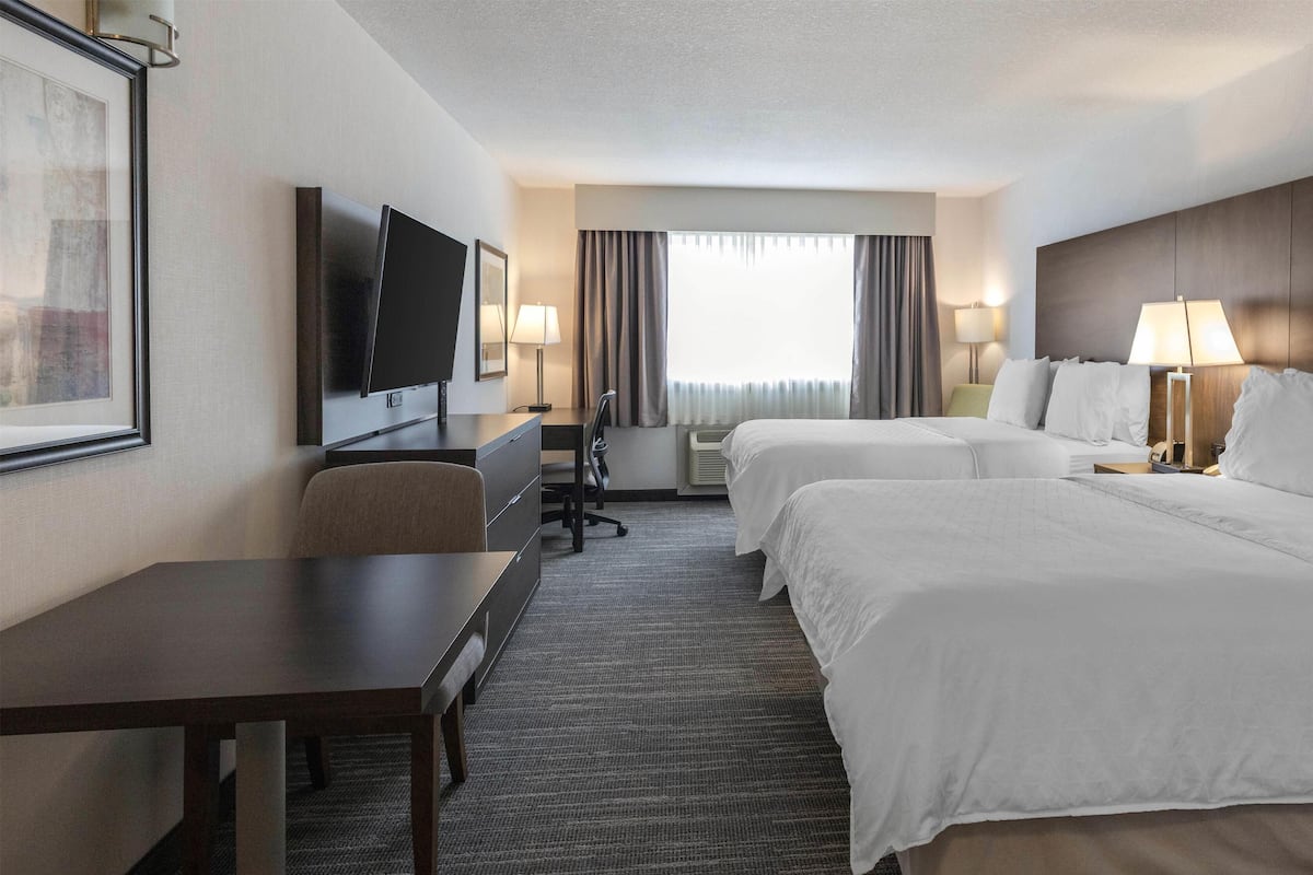 A hotel room with two beds, a desk, a chair, a TV, and a window with curtains.