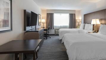 Une chambre d’hôtel avec deux lits, un bureau, une chaise, une télévision et une fenêtre avec des rideaux.