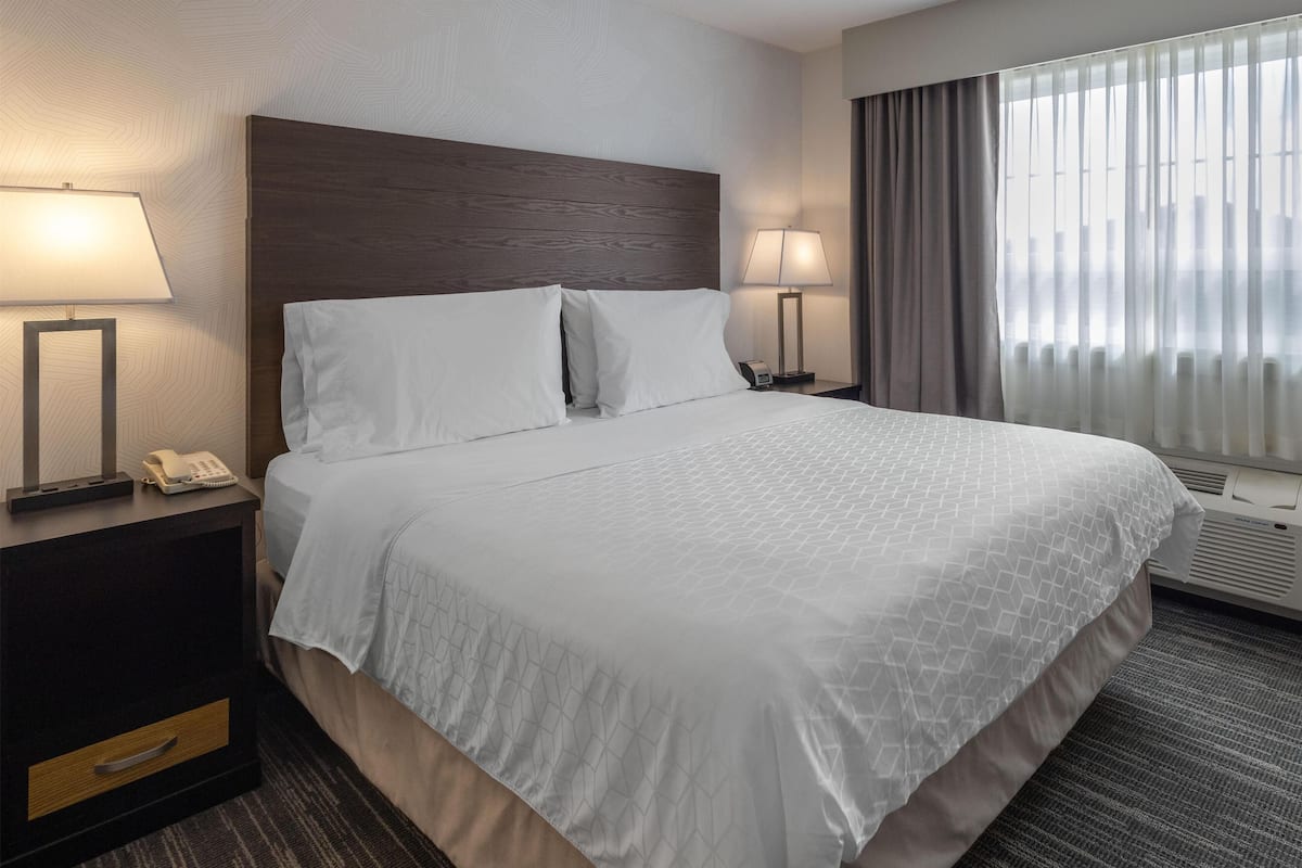 A hotel room with a large bed, two bedside tables with lamps, a phone, and a window with curtains.