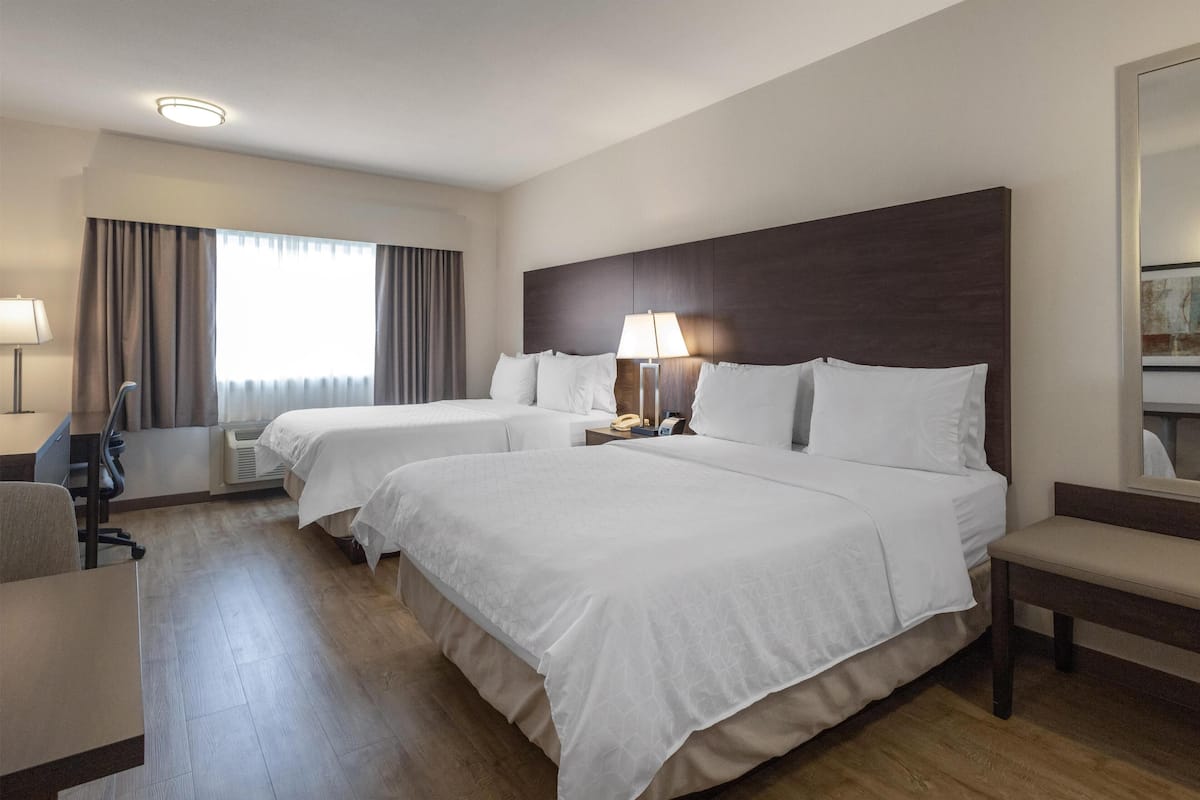 A hotel room with two beds, a desk, a chair, a lamp, and a large window with curtains.