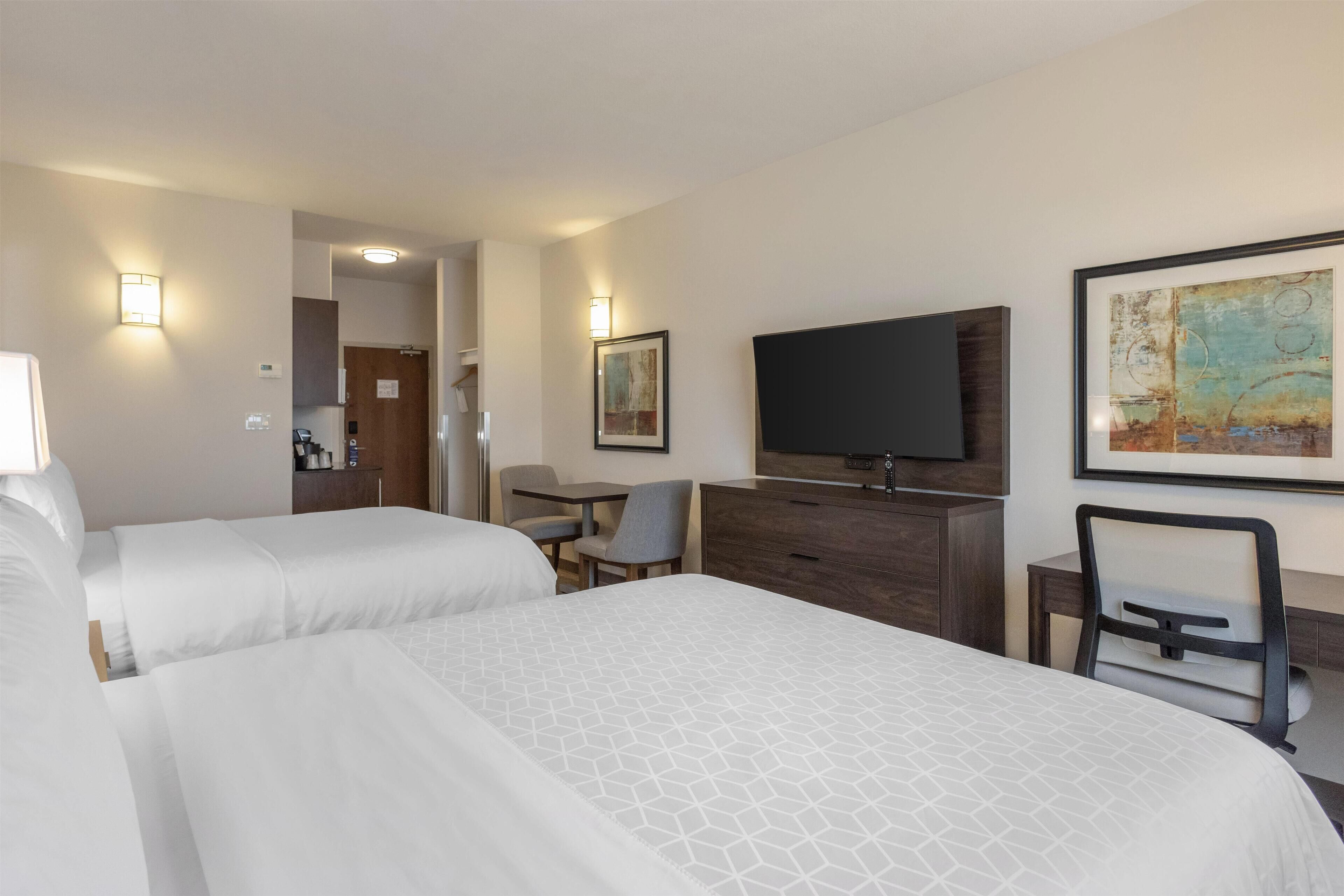 A hotel room with two beds, a desk, a chair, a television, and artwork on the walls.