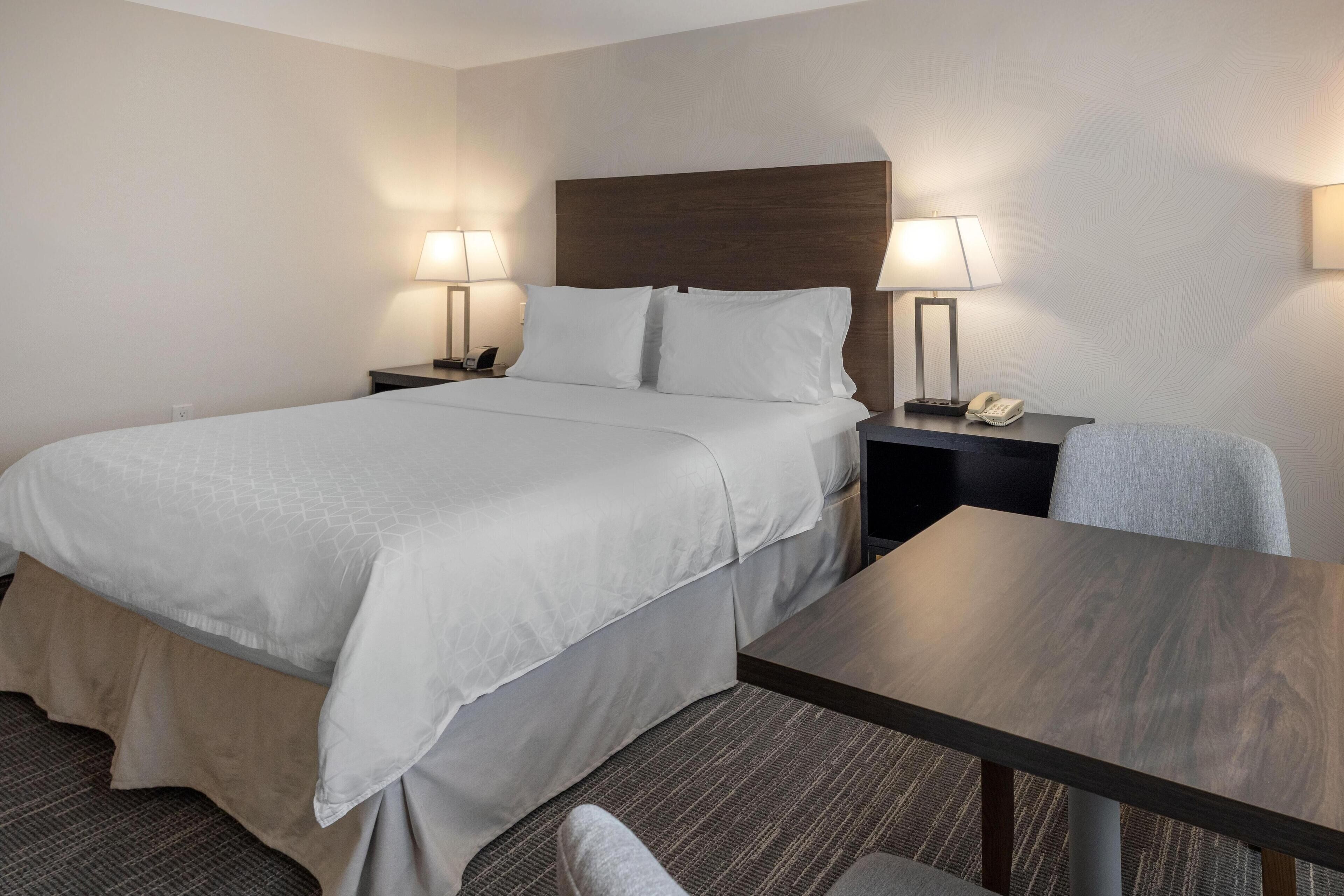 A hotel room with a large bed, two bedside tables with lamps, a small table, and a chair.