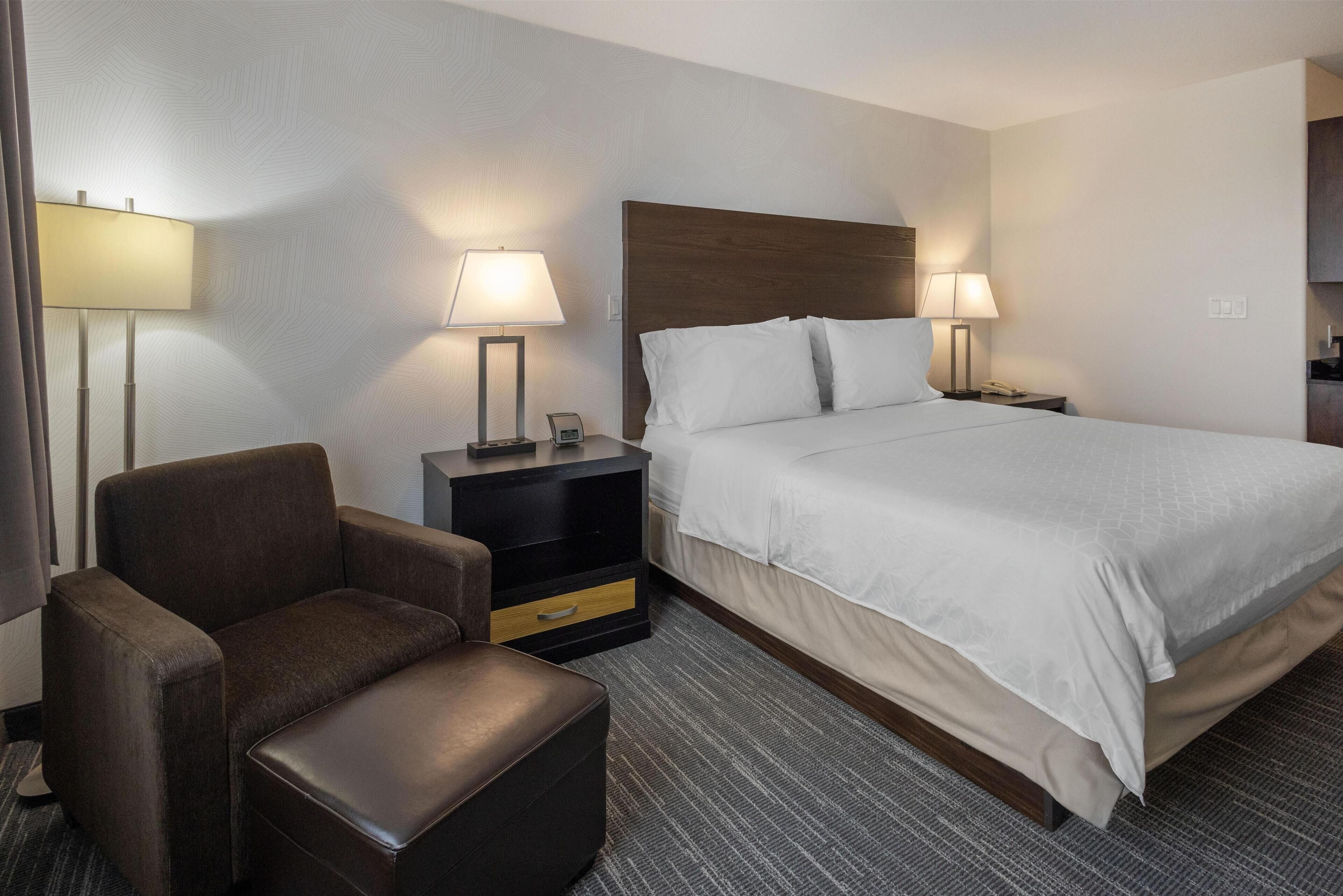 A hotel room with a large bed, two bedside tables with lamps, a chair, and a small desk.