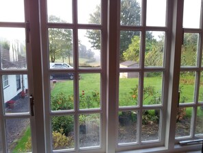 A view through a window with multiple panes, revealing a green lawn, some potted plants, and a parked car outside. - Brambles Bed and Breakfast (Tiverton)