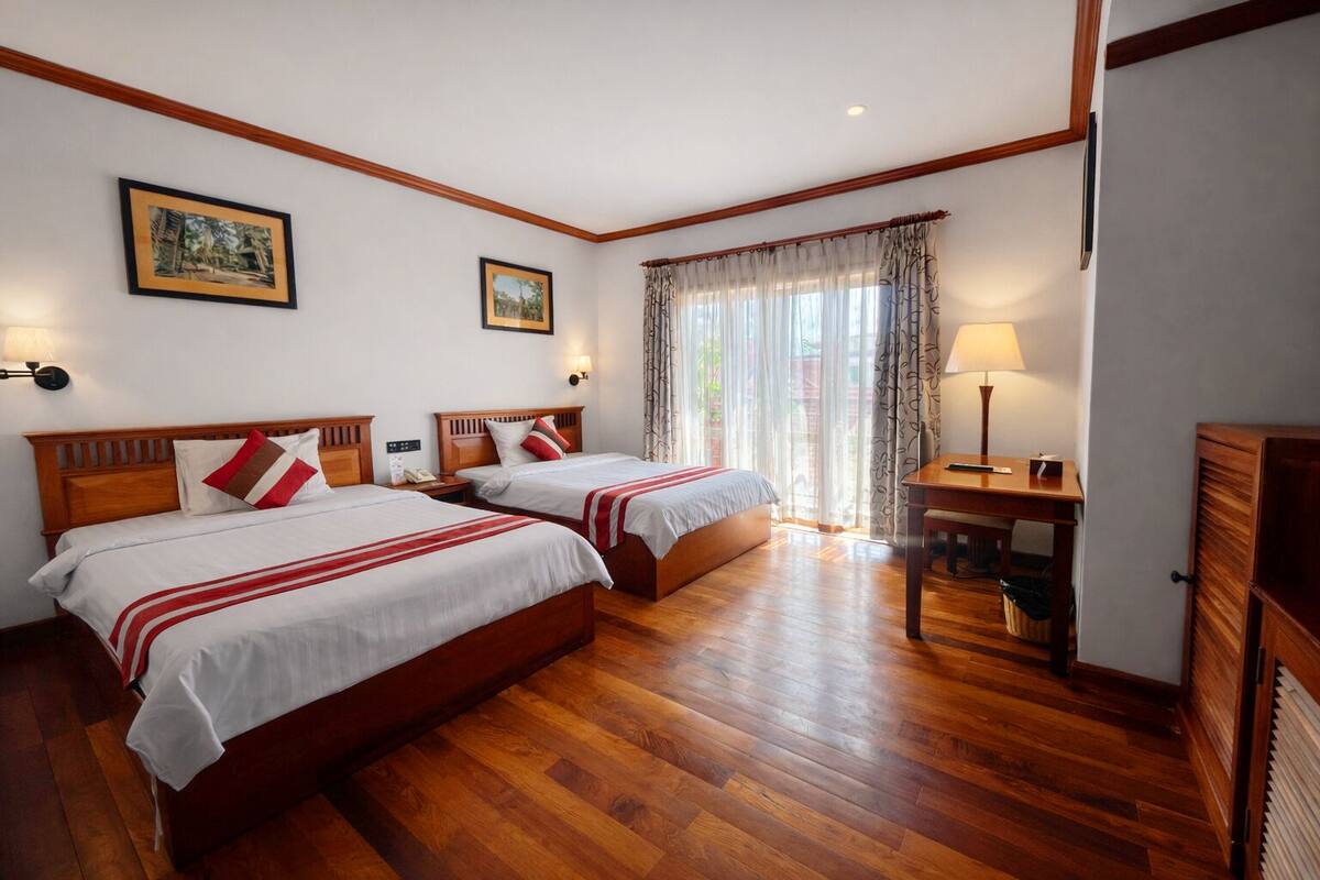 Une chambre d’hôtel avec deux lits, un plancher en bois, un bureau et une fenêtre avec des rideaux.