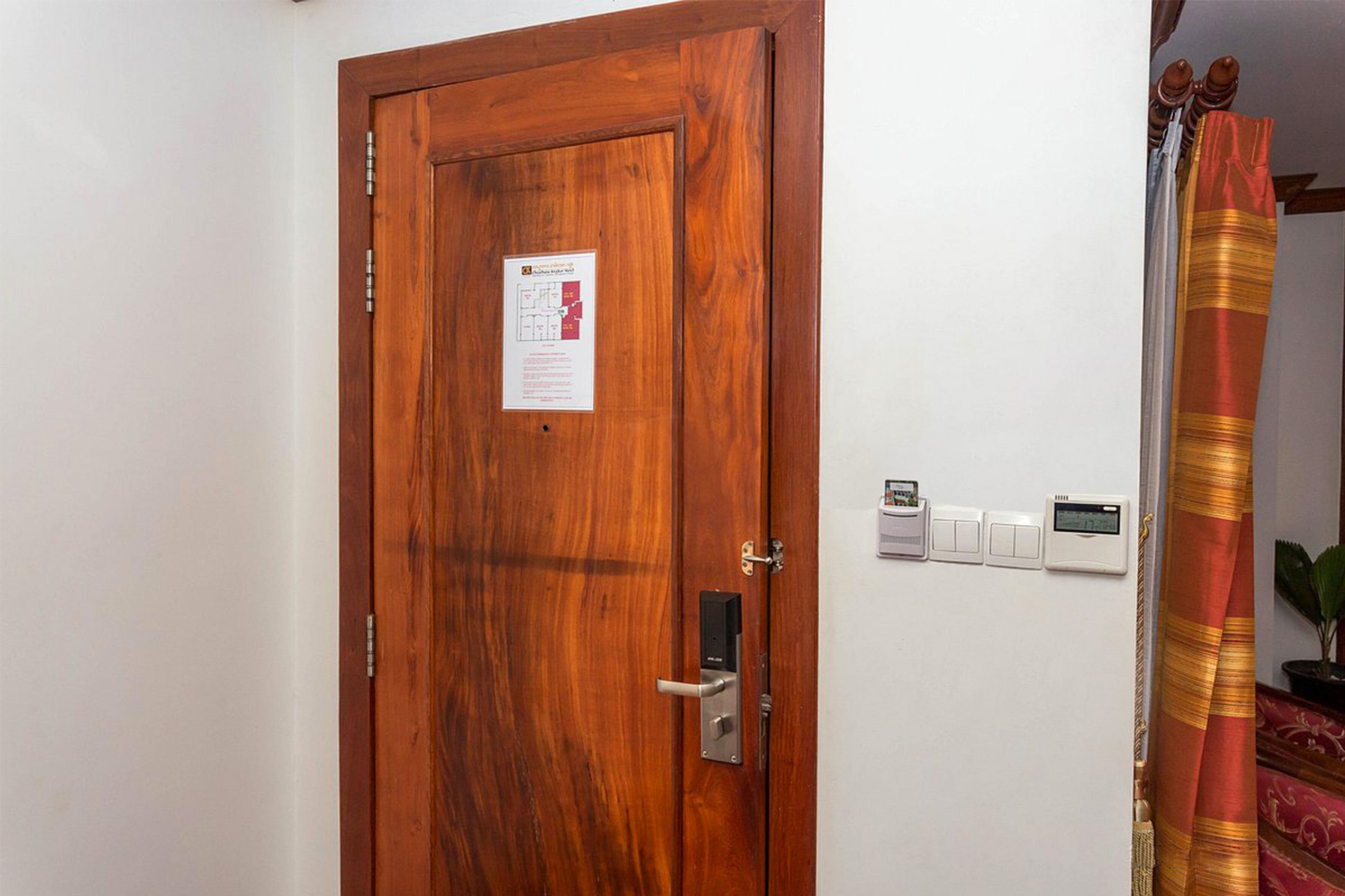 A wooden door with a security lock, a thermostat, and a notice on the wall.