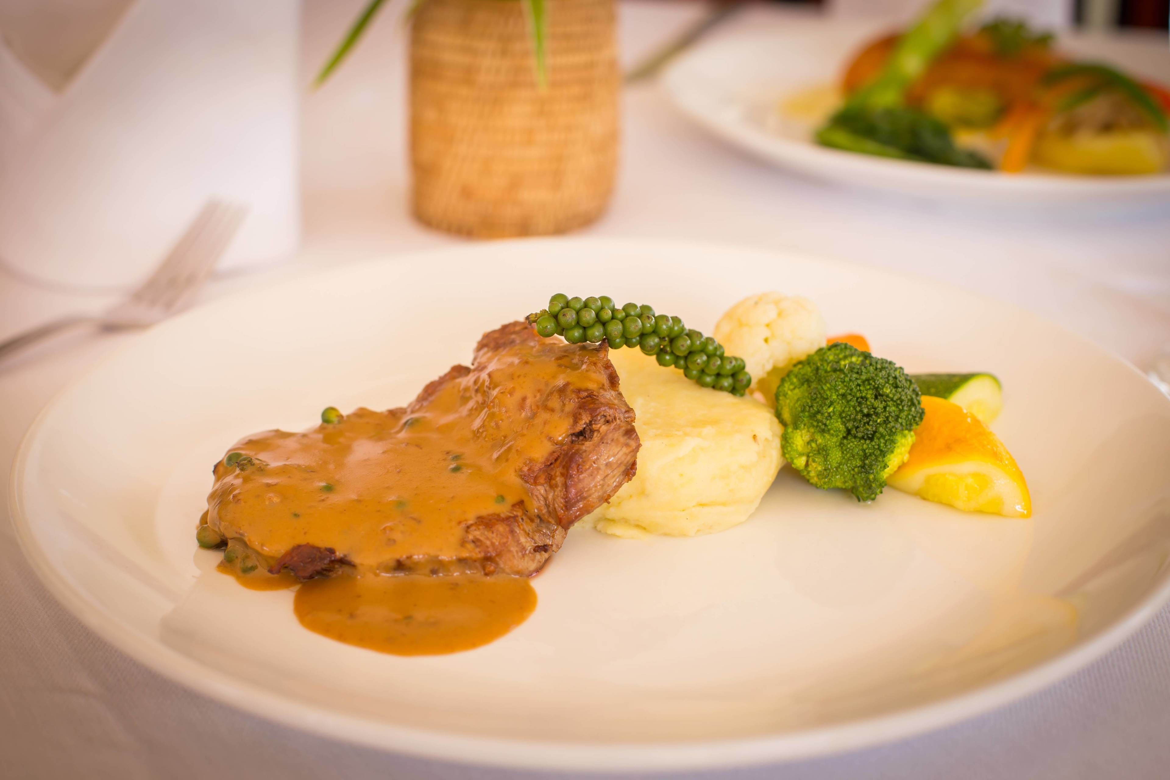 Ein Teller mit einem Steak, Kartoffelpüree, Brokkoli und Orangenscheiben.