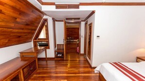 A bedroom with a wooden floor, a bed with a red and white striped bedspread, a wooden bench, and a small table with a mirror. - Cheathata CTA Hotel Siem Reap (Siem Reap)