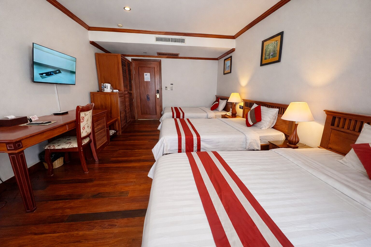 A hotel room with two beds, a desk, a chair, a television, and a door.