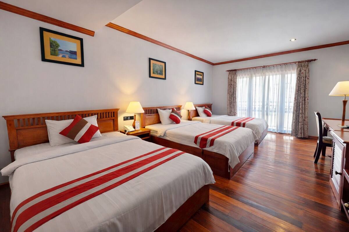 Une chambre d’hôtel avec trois lits, des têtes de lit en bois, des lampes de chevet, un bureau et une chaise.